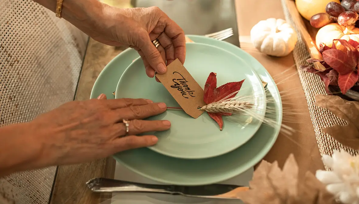 Photo of a place setting on a table decorated for Thanksgiving dinner, with a note on the plate that says "Thank You," representing gratitude
