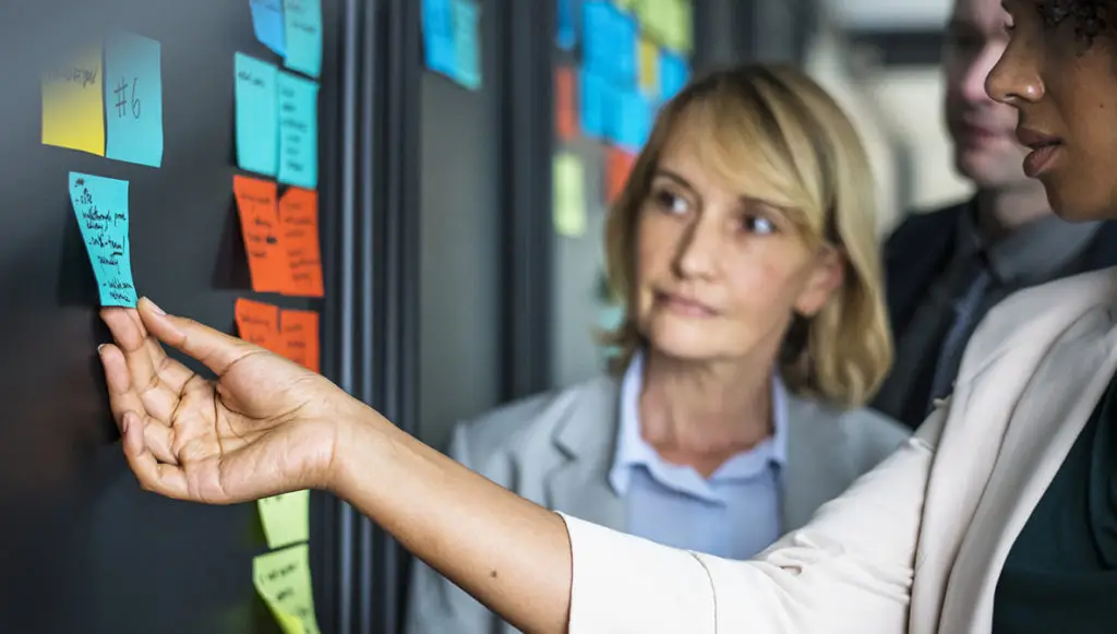Photo of two professional women looking at sticky notes on a board, symbolizing challenges and change