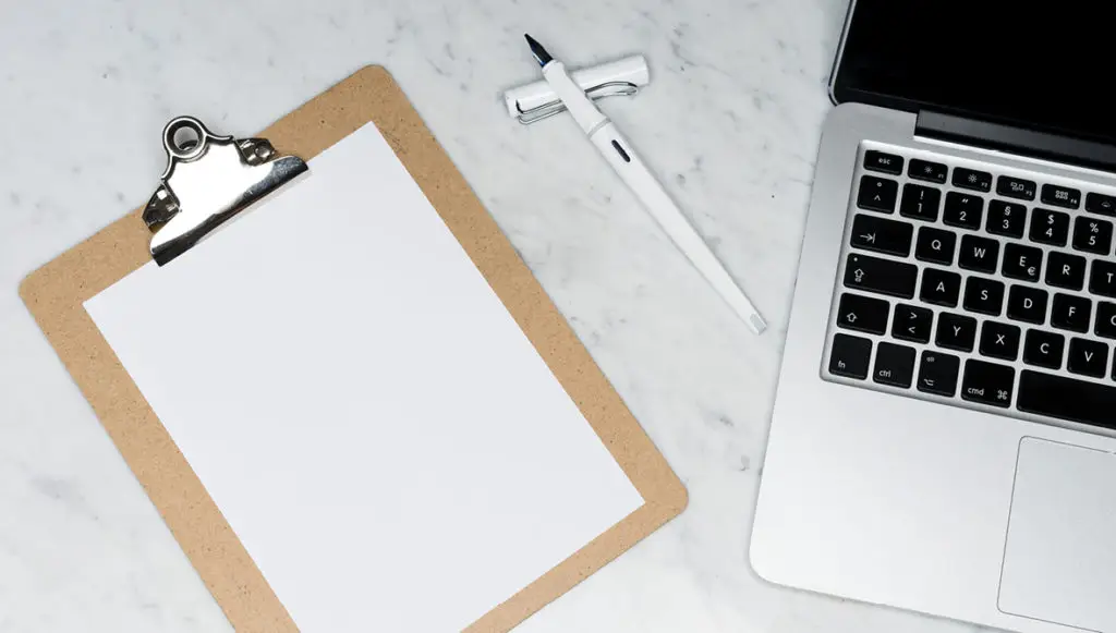 Photo of a clipboard on a desk with a blank piece of paper and a pen