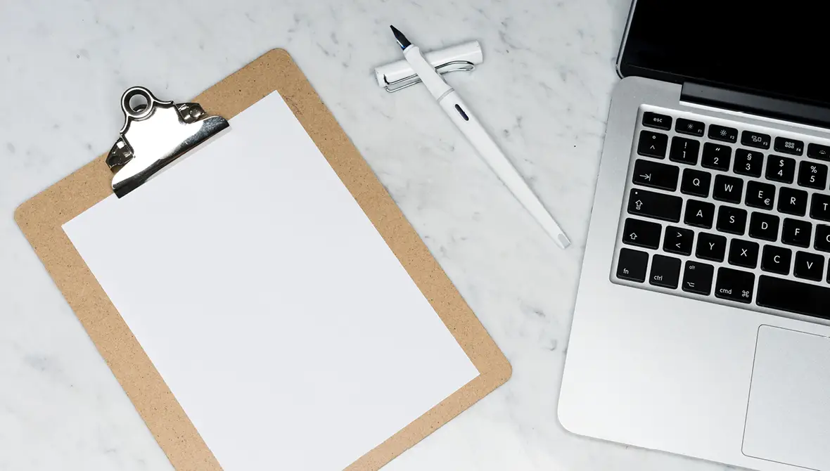 Photo of a clipboard on a desk with a blank piece of paper and a pen