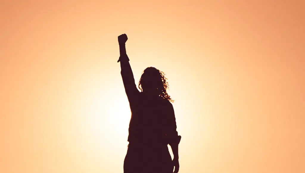 Silhouette of a woman standing with her fist raised
