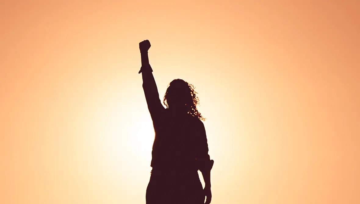 Silhouette of a woman standing with her fist raised