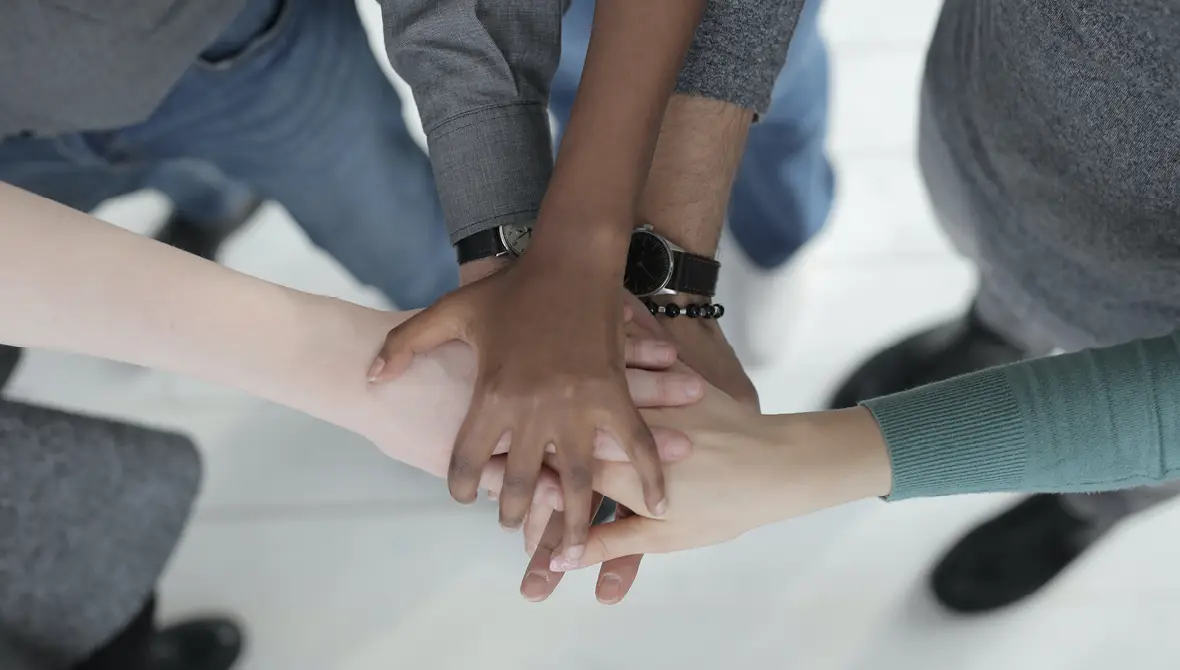 Photo of several people of different races putting their hands together in a huddle. Photo by Andrea Piacquadio.