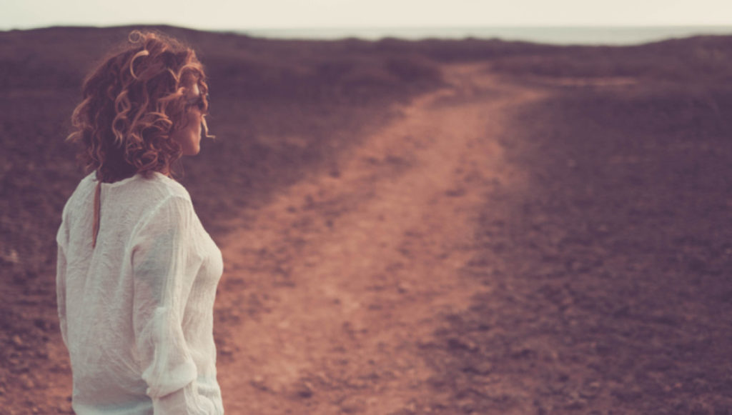 Photo of a woman standing outside looking down a long, dirt road, symbolizing donor journeys