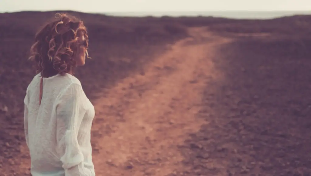 Photo of a woman standing outside looking down a long, dirt road, symbolizing donor journeys