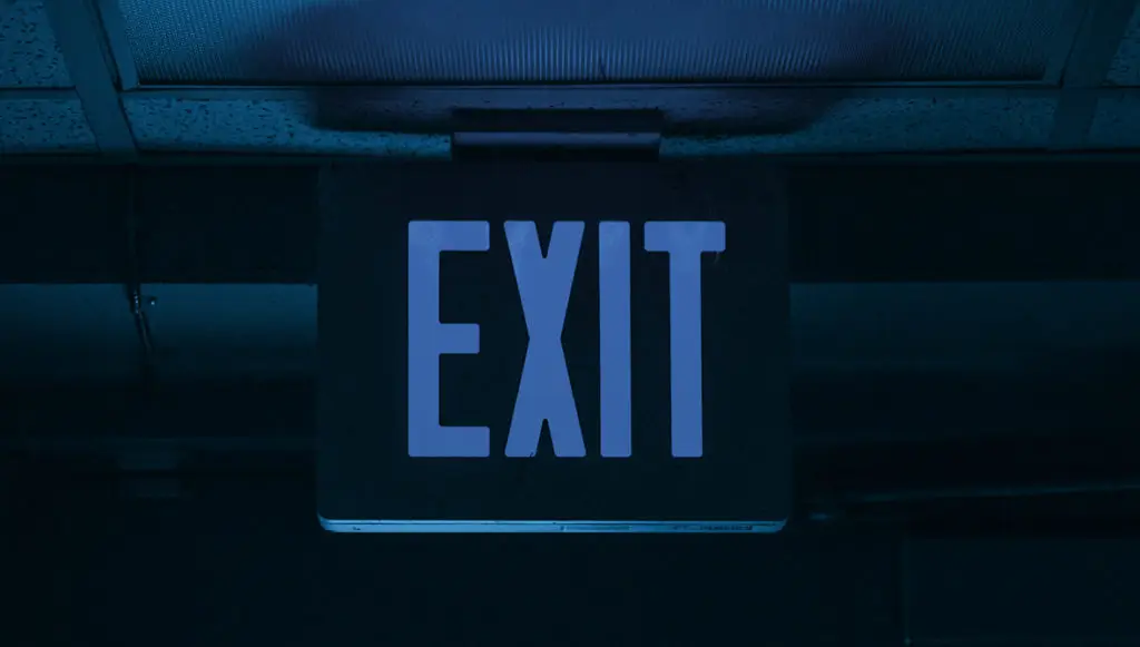 Photo of an EXIT sign hanging from the ceiling of a commercial building