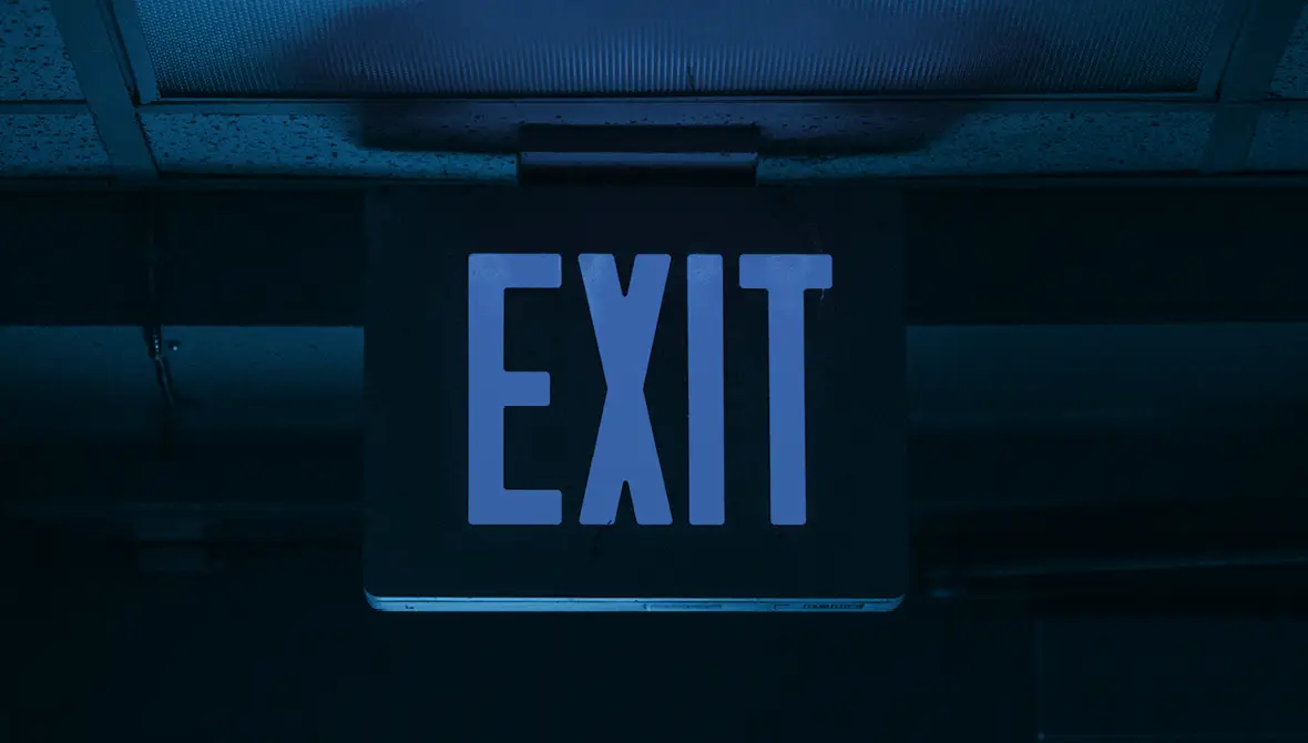 Photo of an EXIT sign hanging from the ceiling of a commercial building