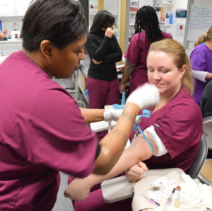 Two females wearing scrubs in phlebotomy training at NewBridge Center for Arts & Technology 