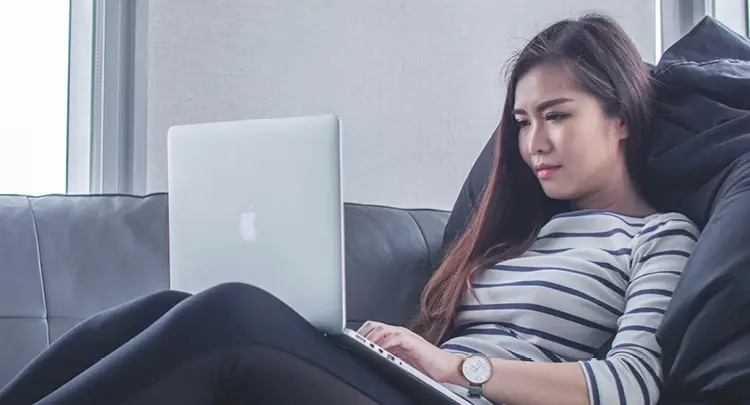 Photo of a woman relaxing on a couch and typing on a laptop, representing professional learning from home