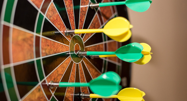 Photo of a dart board with yellow and green darts stuck in it
