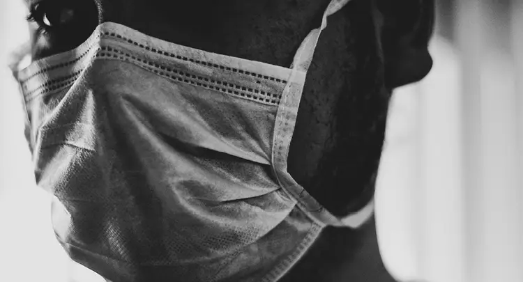 Black & white photo: Closeup of a man's face with a medical mask on