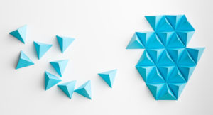 Small, blue folded paper pyramids scattered on a surface coming together to form a larger shape