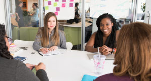 Photo of two young businesswomen sitting at a table in a conference room talking to two other businesswomen