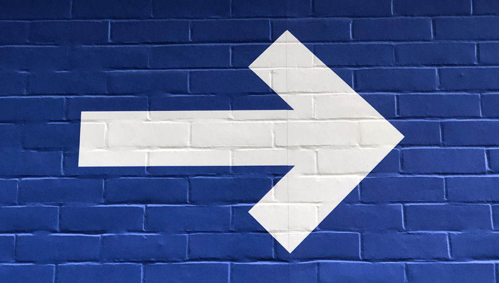 Photo of a brick wall painted blue with a white arrow painted over it