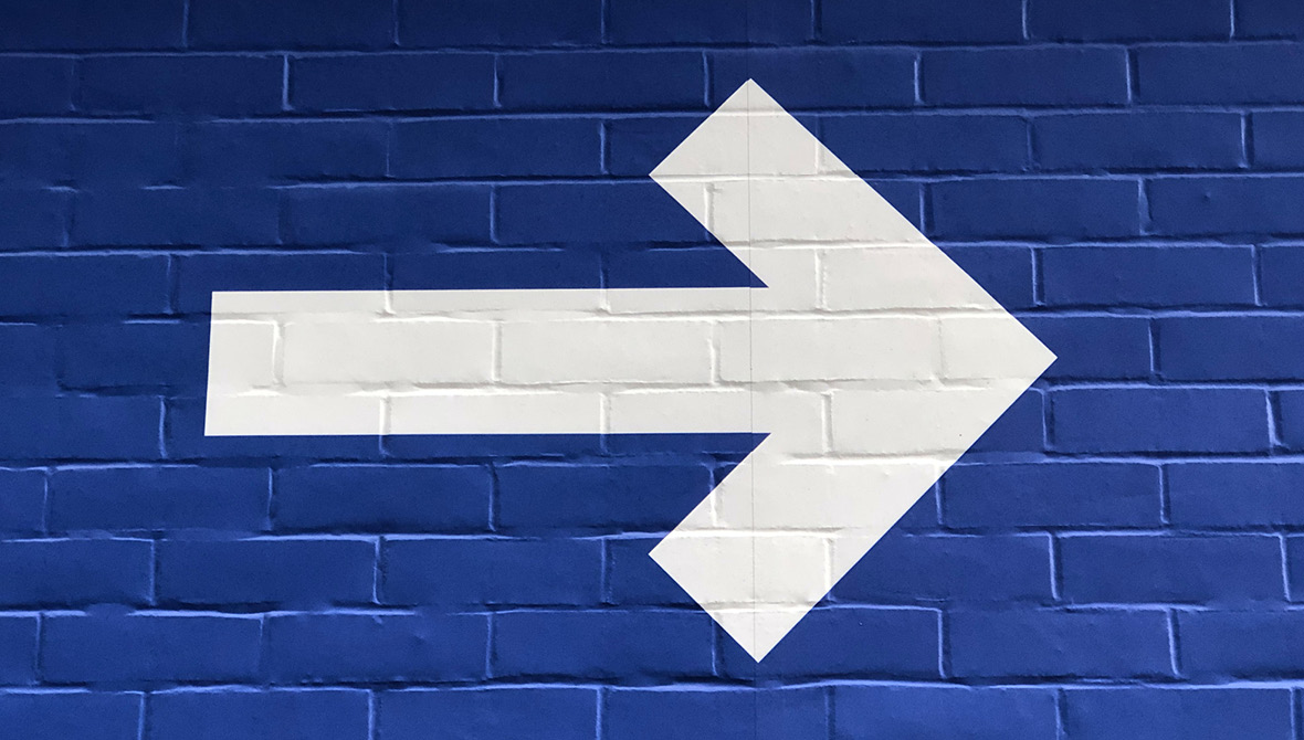 Photo of a brick wall painted blue with a white arrow painted over it