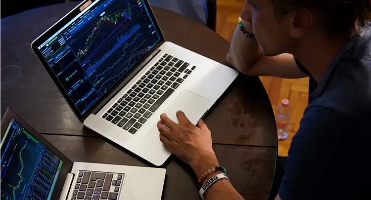 Photo of a man sitting at a table with two laptops, each showing charts of data.