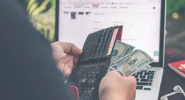 Photo: Close-up of a woman's hands pulling one hundred dollar bills out of a wallet
