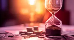 Photo of an hourglass on a table with small stacks of coins and dollar bills next to it