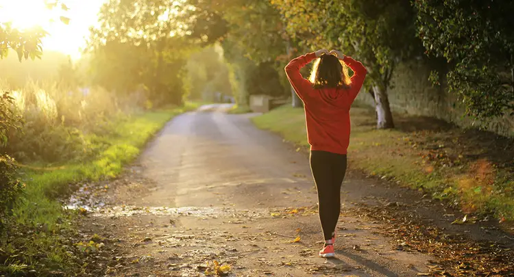 Photo of a woman in athletic wear walking down a dirt road lined with trees, symbolizing one type of self-care