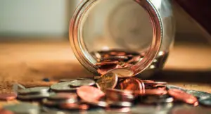 Photo of a glass jar overturned on a table with coins spilling out