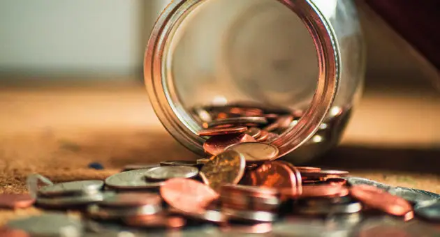 Photo of a glass jar overturned on a table with coins spilling out