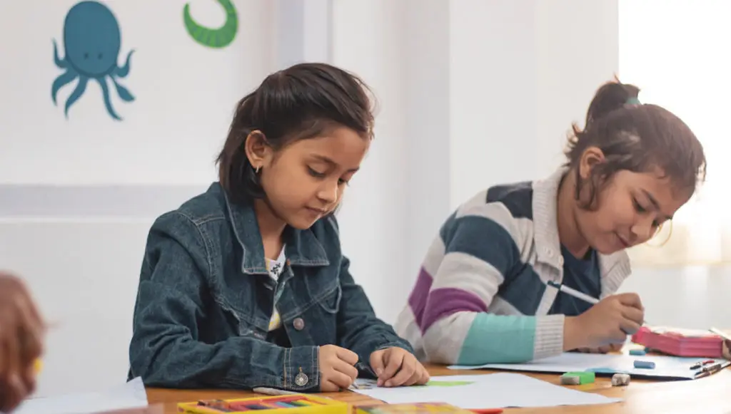 Photo of two female elementary school students drawing with colored pencils at a table