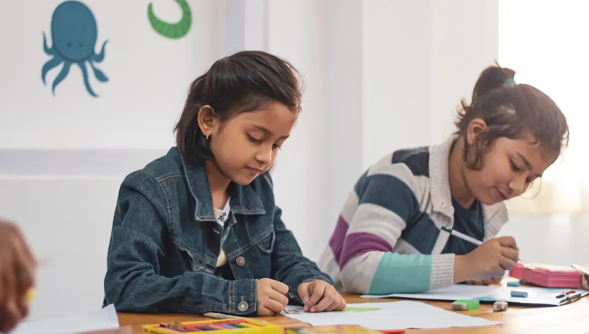 Photo of two female elementary school students drawing with colored pencils at a table