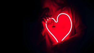 Photo of a woman standing in the dark holding a heart-shaped neon light