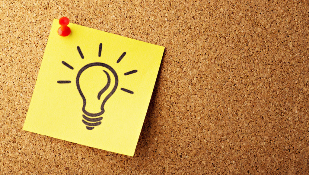 Photo of a yellow sticky note with a picture of a light bulb drawn on it pinned to a cork board