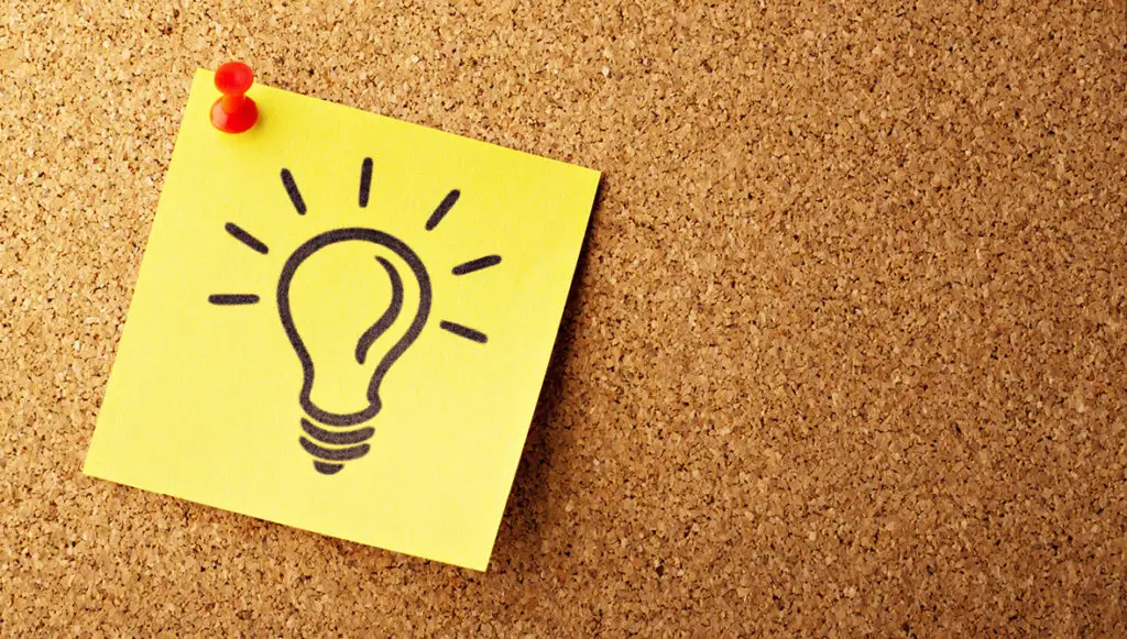 Photo of a yellow sticky note with a picture of a light bulb drawn on it pinned to a cork board