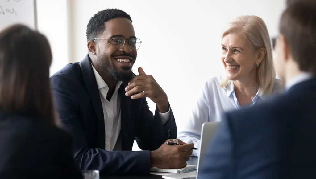 Photo: Diverse group of business professionals sitting at a conference table chatting and smiling
