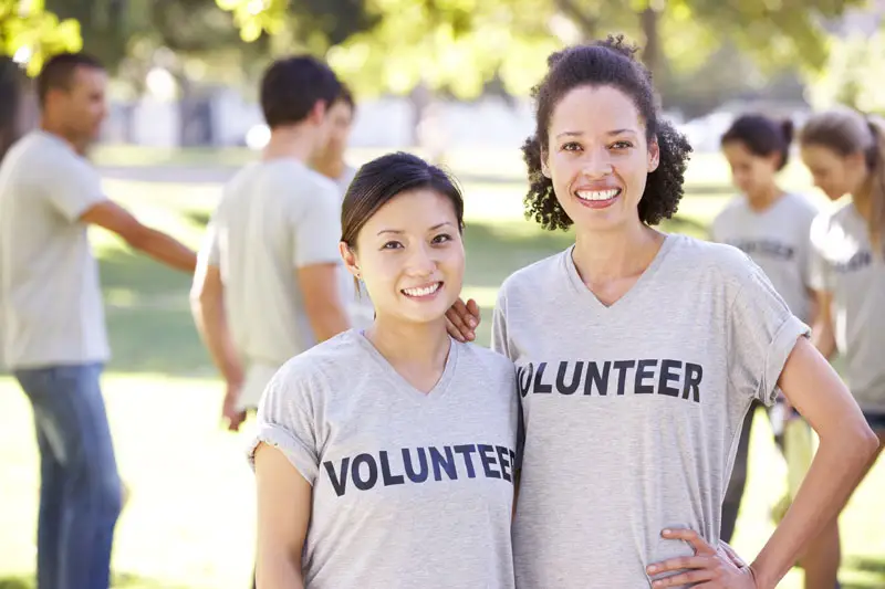 Photo of two adult women standing outside wearing t-shirts that say "VOLUNTEER," representing local action