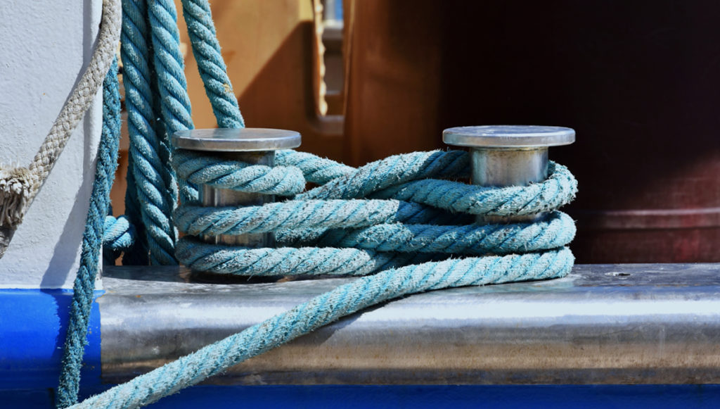 Photo of light blue sailing ropes securely coiled around metal posts