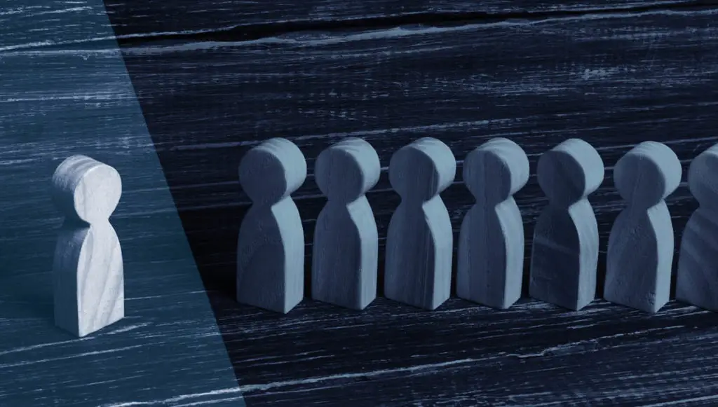 Group of wooden figures positioned in a line with one single figure standing apart from the others, representing the concept of exclusion in grant eligibility