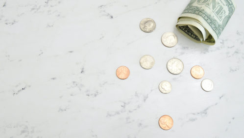 Photo of several U.S. coins and a single dollar bill scattered across a large counter, symbolizing a decline in household giving (photo credit: Katie Harp, Unsplash)