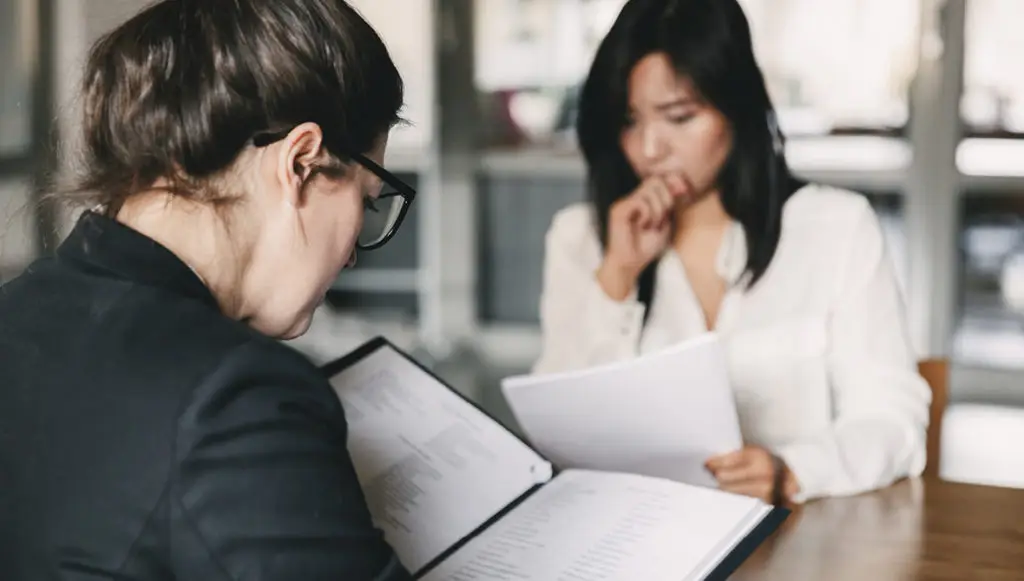 Photo of two businesswomen at a conference table, each looking at a portfolio of grant information