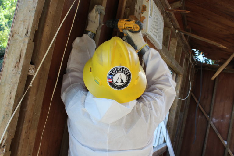 Photo of a Conservation Corps worker using a power tool on the studs of an interior wall.