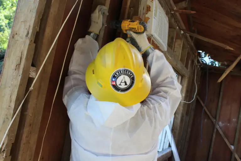 Photo of a Conservation Corps worker using a power tool on the studs of an interior wall.