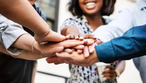 Close-up photo of a group of adults putting their hands together as a team, representing a giving circle