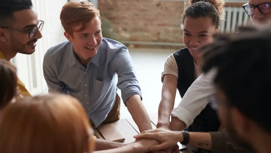 A group of smiling teens stand in the center of a classroom talking with their teacher and each other (representing youth philanthropy)