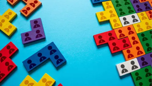 Photo shows two sets of colorful wooden blocks on a table. One set is neatly organized in rows and columns while the other set of blocks is scattered and waiting to be organized in some way, representing different organizational structure models.