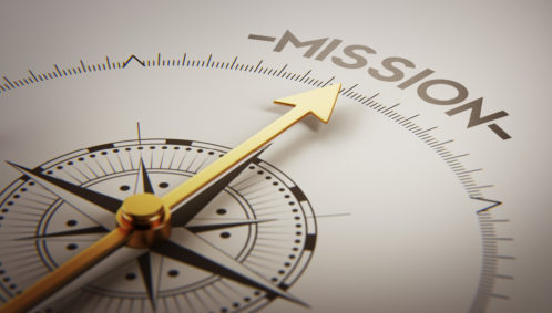 Close-up photo of a compass with the arrow pointing to the word "MISSION" (meant to represent the concept of mission accountability)