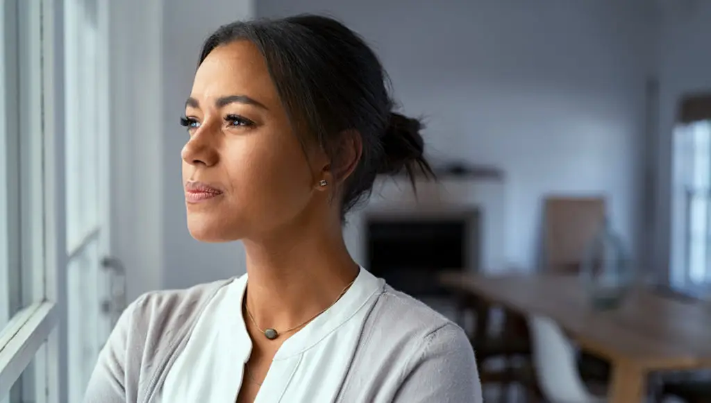 A professional woman looks out a window in thought, as if rethinking capacity building.