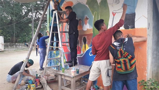 Six young people work together to paint a mural on the side of a building in Oaxaca.