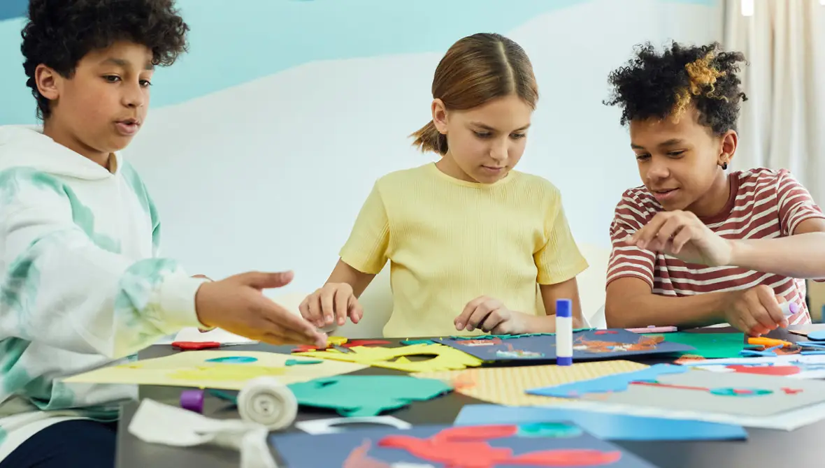 Three young students working together on art projects in a classroom