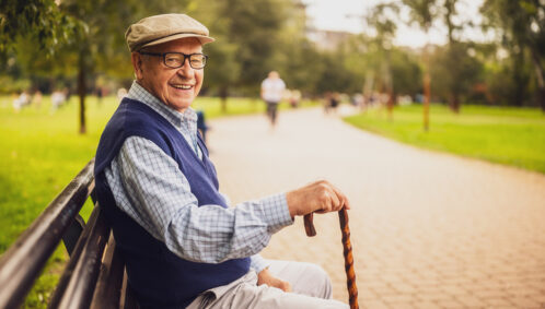 A smiling, aging man sits on a park bench