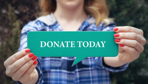 A woman holds a small green sign that reads, "Donate Today"