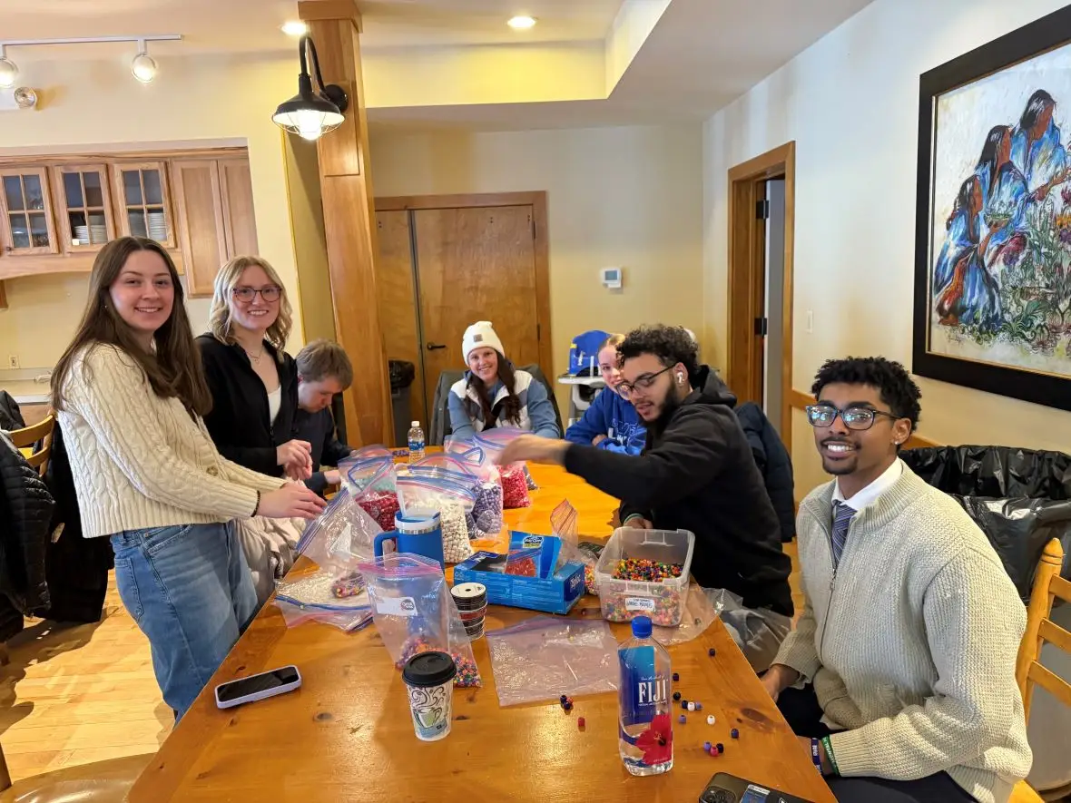 A group of seven student volunteers around a tabling sorting beads for a children's craft program