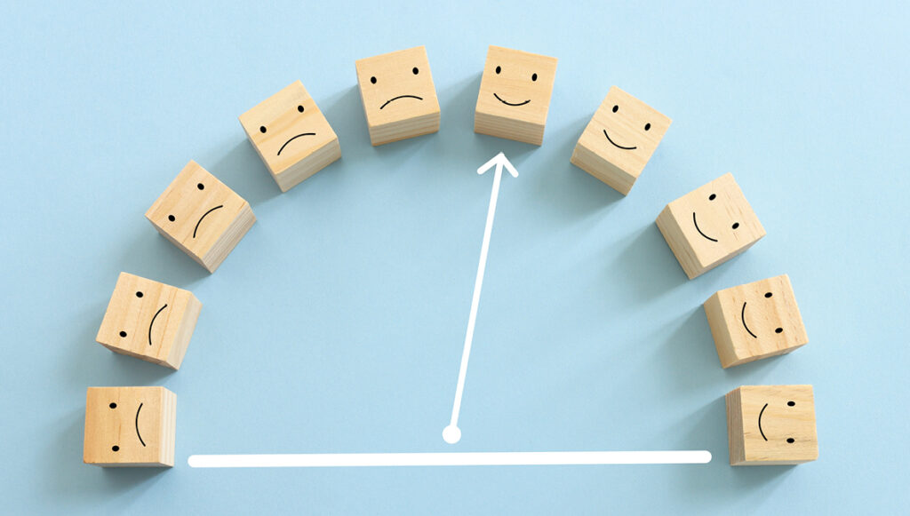Wooden blocks laid out in an arc feature sad faces on some and happy faces on others. A white arrow points to one of the happy faces.