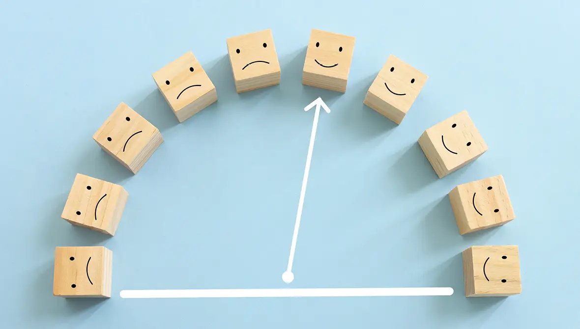 Wooden blocks laid out in an arc feature sad faces on some and happy faces on others. A white arrow points to one of the happy faces.